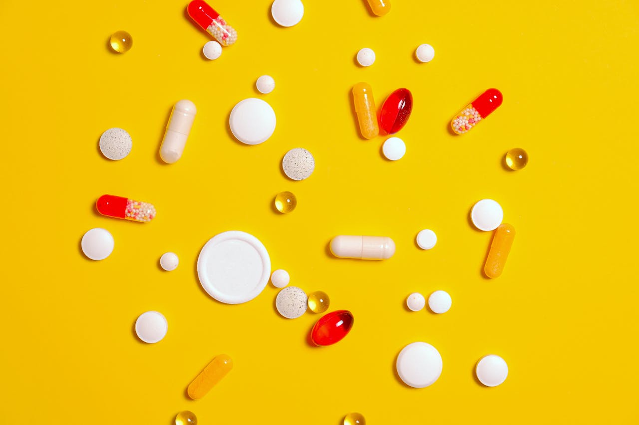 A variety of pills and capsules scattered on a vibrant yellow backdrop, emphasizing health and medicine.
